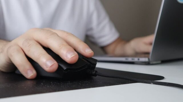 Close-up of a hand using a computer mouse while working on a laptop at a desk