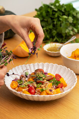 A person prepares a vibrant vegan salad with roasted pumpkin, tomatoes and chickpeas