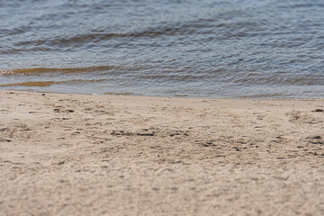 Overcast beach scene with sloping sand, footprints, and small choppy waves Natural color palette sandy beige, blue-gray water, greenish shoreline Serene atmosphere, realistic style, distant perspe