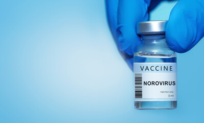 Doctor in protective medical gloves carefully holding a Norovirus vaccine vial against a clean blue background,symbolizing modern medicine, immunization awareness, disease prevention,global healthcare