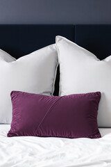 plush purple pillow on crisp white bedding with navy headboard