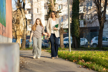 Obraz premium A mother takes her daughter to school. They walk together along the school path, holding hands.