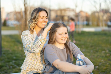 Naklejka premium A casual yet heartfelt moment of a mother braiding her daughter’s hair while both enjoy a calm afternoon in the park.