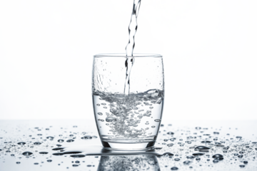 Fresh water being poured into a clear glass creating ripples and splashes on a reflective surface in a bright setting