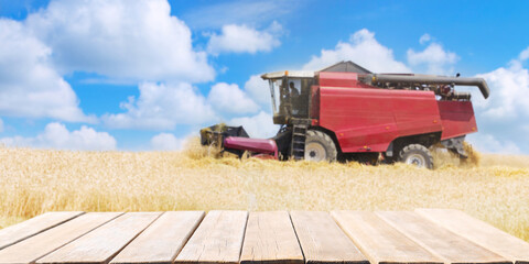 empty wooden table and combine harvester working in wheat field in a summer day