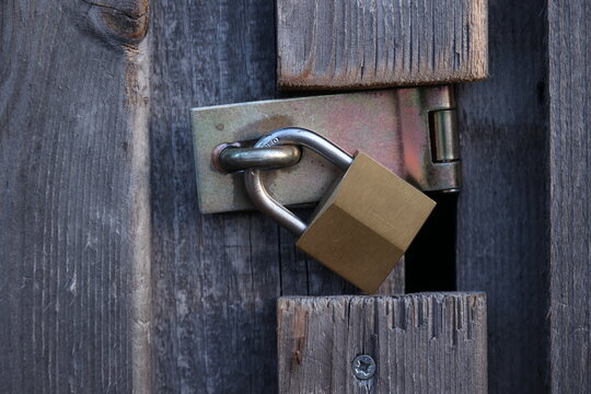 A gold padlock is hanging from a wooden door