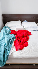 unmade bed with red and teal duvet white pillows and a box