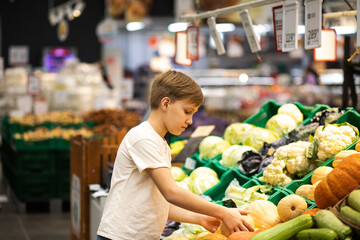 Kid teenager shopping for fresh organic fruits and vegetables in supermarket. Cute boy holding pumpkin in a hands.