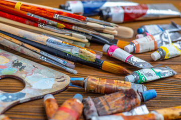 Old used brushes and paint tubes in an artist's studio, palette with multi-colored spots of oil or...