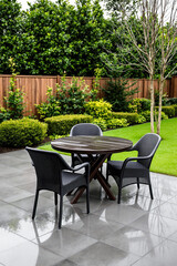 Fototapeta premium dark brown round table and four black wicker chairs on wet stone patio