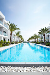 Fototapeta premium long blue swimming pool at a tropical resort with palm trees and modern white buildings