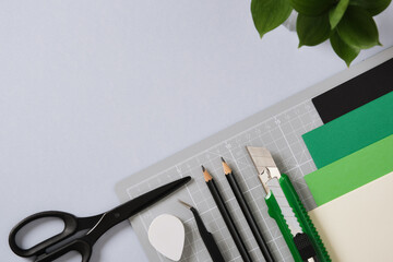 Paper crafting tools: scissors, craft knife, pencil, tweezers, eraser, cutting mat, paper on gray background. Place for your text.