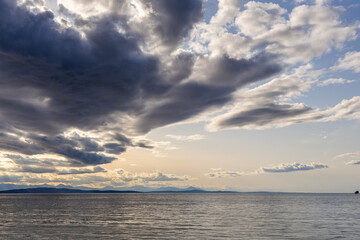 Obraz premium Dramatic Cloudscape Over Ocean With View of Distant Mountains and Calm Waters
