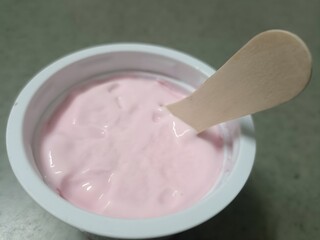 A close-up of creamy pink yogurt in a white cup with a wooden stick. Smooth, sweet, and refreshing—perfect for a light snack or a delightful dessert moment.