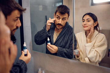 Reflection in mirror of a couple applying face cream.