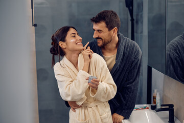 Embraced couple having fun with face cream in bathroom.