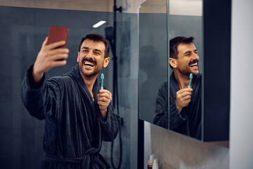 Happy man taking selfie while brushing his teeth in bathroom.