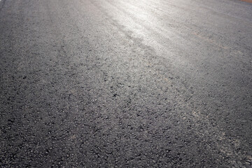 A close-up view of a freshly laid asphalt surface, showcasing a dark gray color with a slightly reflective sheen. Small aggregates are visible, enhancing texture.