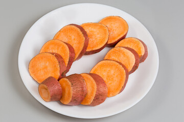 Raw sweet potato tuber sliced into circles on dish