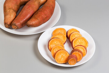 Sliced raw sweet potato tuber against whole tubers on dishes