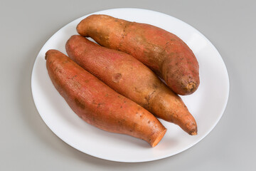 Raw sweet potato tubers on dish on gray background