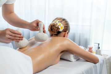 Hot herbal ball spa massage body treatment, masseur gently compresses herb bag on woman body....