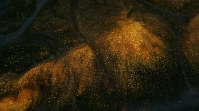 Glitter fluid. Shimmering spill. Golden powder particles paint emerge swirl flowing in black gray gel emulsion art abstract background.