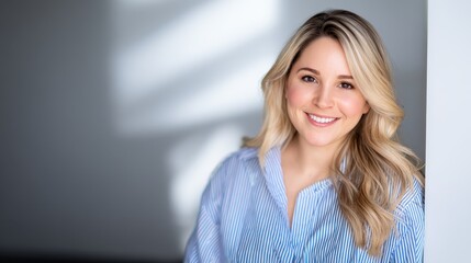 Smiling woman in a striped shirt poses gracefully near a wall with soft shadows