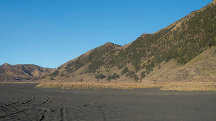 Scenic view of Mount Bromo landscape in East Java, Indonesia. Volcanic hills, black sand desert, and clear blue sky. Popular tourist destination for trekking, nature, and adventure travel.