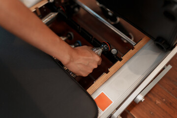 Close up, Hand of athletic adjusts spring resistance on Pilates reformer in modern studio. Fitness concept, pilates training, wellness lifestyle, healthy exercise routine.