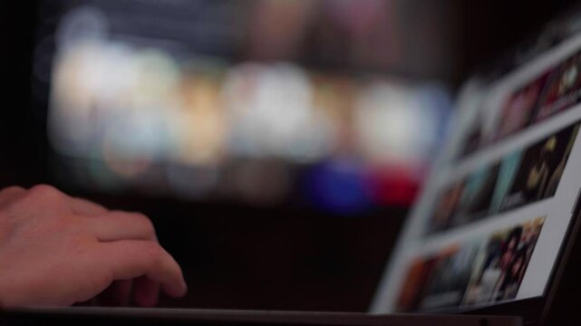 Hand browsing streaming movie selections on laptop screen while navigating entertainment choices, scrolling through movie options on a streaming service on a laptop, choosing what to watch