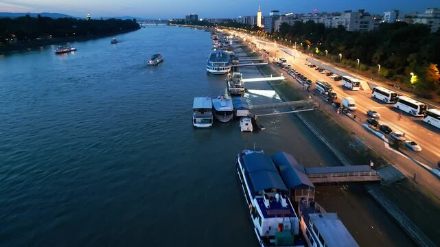 4K drone aerial night video of the Danube riverside in Budapest, Hungary with tourist boats docked along the shore, illuminated streets under city lights