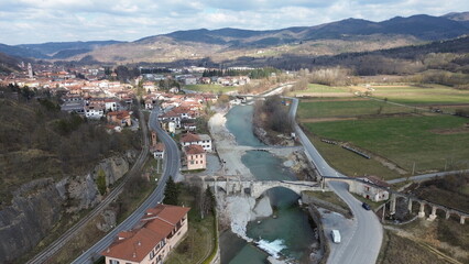 Breathtaking aerial view of the blue water Tanaro river flowing through the green hills of the countryside and the Roman bridge near Bagnasco city in the province of Cuneo