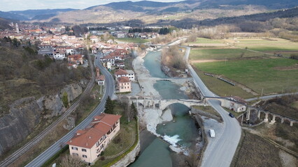 Breathtaking aerial view of the blue water Tanaro river flowing through the green hills of the countryside and the Roman bridge near Bagnasco city in the province of Cuneo