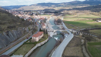 Breathtaking aerial view of the blue water Tanaro river flowing through the green hills of the countryside and the Roman bridge near Bagnasco city in the province of Cuneo