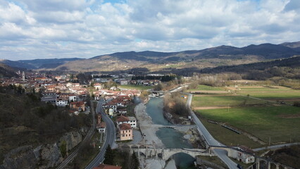 Breathtaking aerial view of the blue water Tanaro river flowing through the green hills of the countryside and the Roman bridge near Bagnasco city in the province of Cuneo
