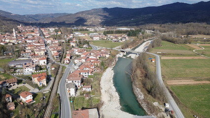 Breathtaking aerial view of the blue water Tanaro river flowing through the green hills of the countryside and the Roman bridge near Bagnasco city in the province of Cuneo