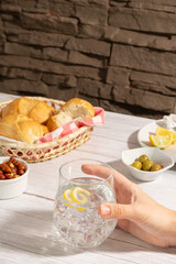 Hand holding a sparkling beverage with a lemon twist on ice sitting on a white wooden table. The...