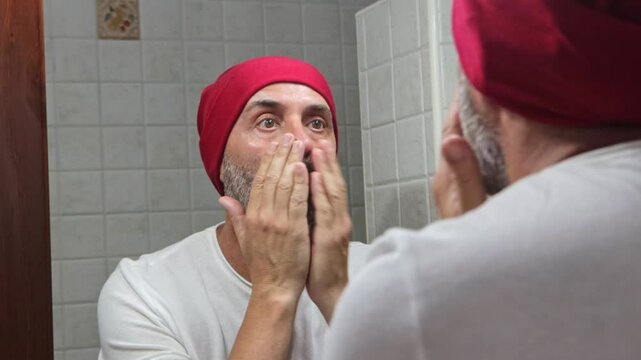 A mature man applying facial cream to his beard in the mirror. Focused on beard care, demonstrating personal hygiene and wellness habits.