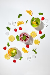Three glasses with orange and berry lemonades. Orange slices, strawberries, mint leaves and ice cubes lie around on a white background. Top view