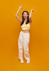 Happy young asian woman listening to music with headphone and dancing isolated on yellow background. People lifestyle relax concept.