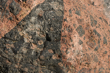 Stone block of red-black color from cemented rock fragments in the bed of a mountain river. Natural background.