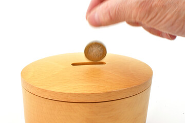 Coing being dropped into the slot of a wooden money box with slow shutter speed to blur the motion of the coin