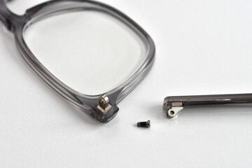 Close up view of the broken arm of a pair of glasses with a small screw alongside