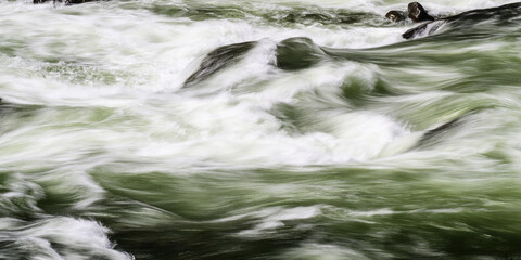 River rages in whitewater shapes in long exposure with green waves