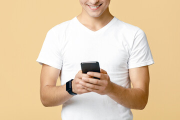 Modern communication, chat in social networks and mobile app. Cheerful cute young guy student with glasses typing on mobile smartphone in blog, isolated on beige background, studio shot, free space