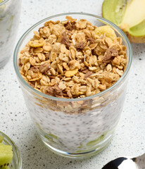 Glass filled with chia seed pudding, layered with diced kiwi at the bottom and topped with crunchy granola