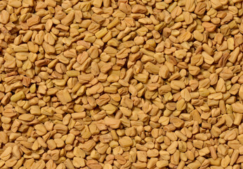 A detailed, top down close up of a dense pile of dry, light brown fenugreek seeds