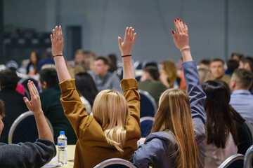 Attendees in a seminar actively participate by raising hands to engage in discussions.