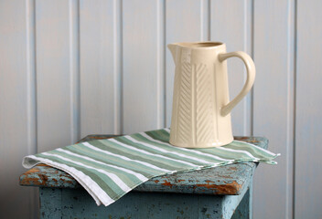 Cream pitcher sitting on striped cloth on rustic table